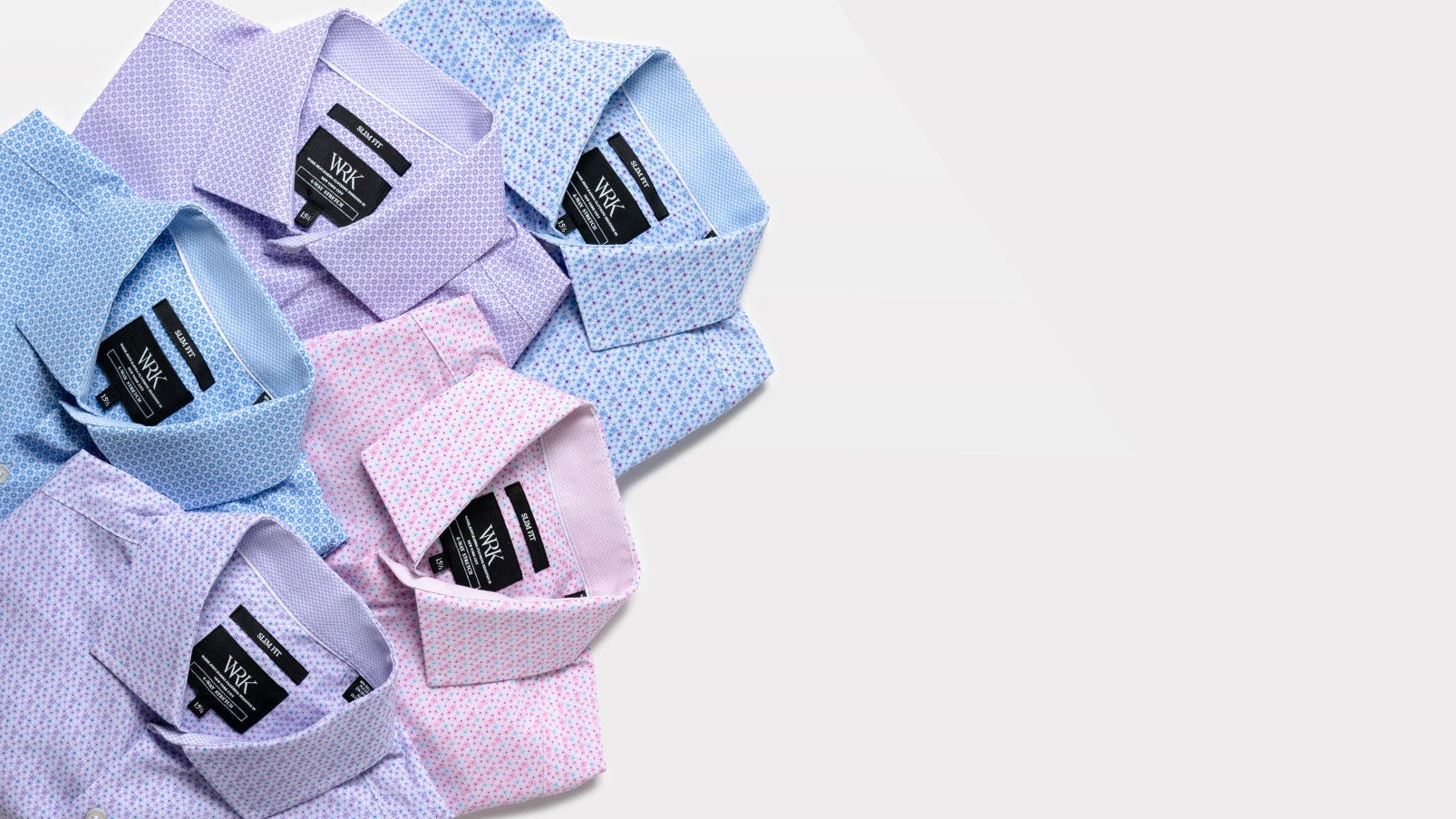 Four men's dress shirts in light blue, lavender, and pink, arranged diagonally on a clean white background. The shirts feature subtle textured patterns and are shown from a top-down angle, highlighting their collars and inner neck labels.