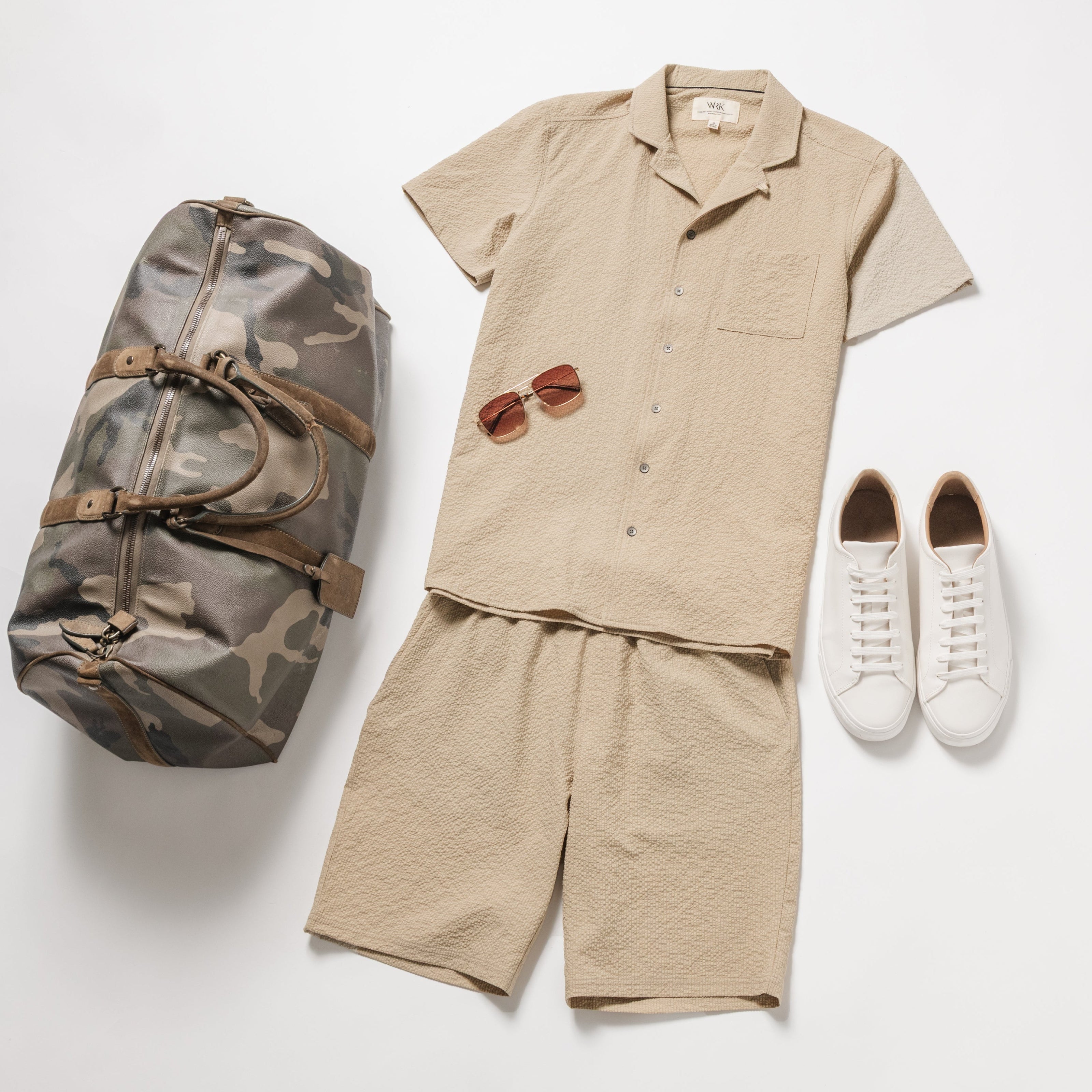 Beige shirt, shorts, white sneakers, camouflage bag, and sunglasses on a white background